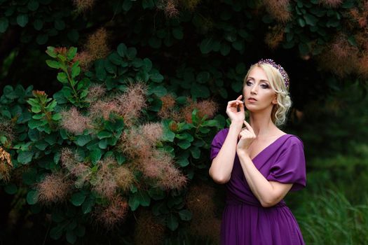 Girl model blonde in a lilac dress with a bouquet with a green forest