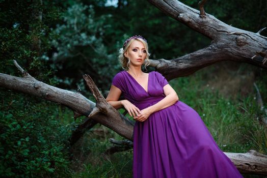 Girl model blonde in a lilac dress with a bouquet with a green forest