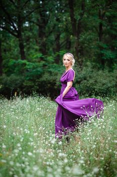 Girl model blonde in a lilac dress with a bouquet with a green forest