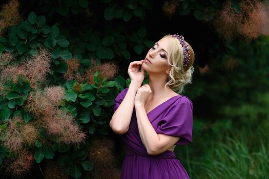 Girl model blonde in a lilac dress with a bouquet with a green forest