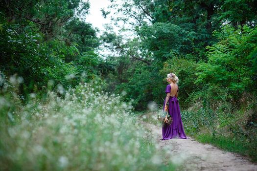 Girl model blonde in a lilac dress with a bouquet with a green forest