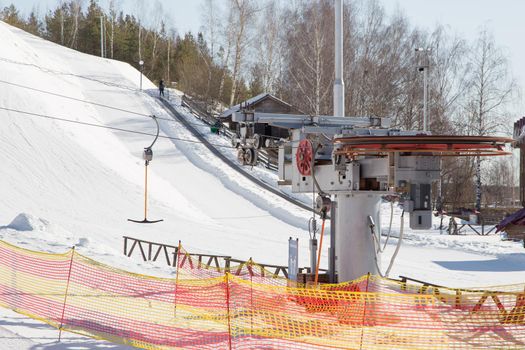 Rotating cable car lift in a ski resort. Lighting pillars and trees against the blue sky. Mountain slope equipment for snowboarding. Ski tours on a sunny day.