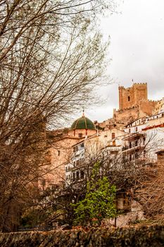 Beautiful overview of the town of Alcala de Jucar with the fortress castle and the church in spring under gray sky