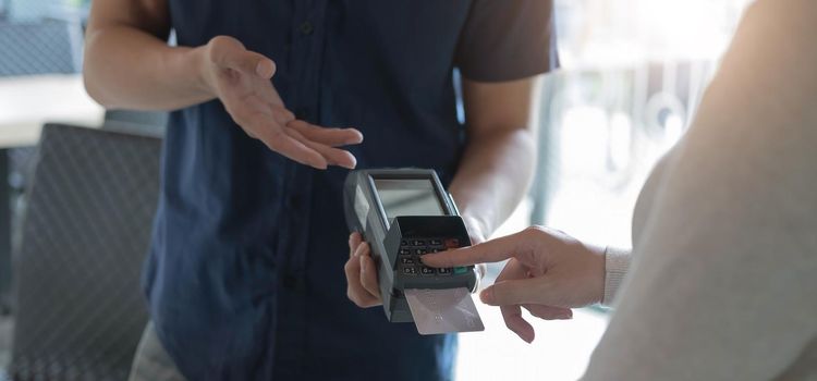 Woman paying by credit card and entering pin code on reader holded in coffee. Customer using credit card for payment. Mature cashier accepting payment over nfc technology..