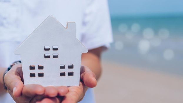 Hand holding wooden home model on beach background