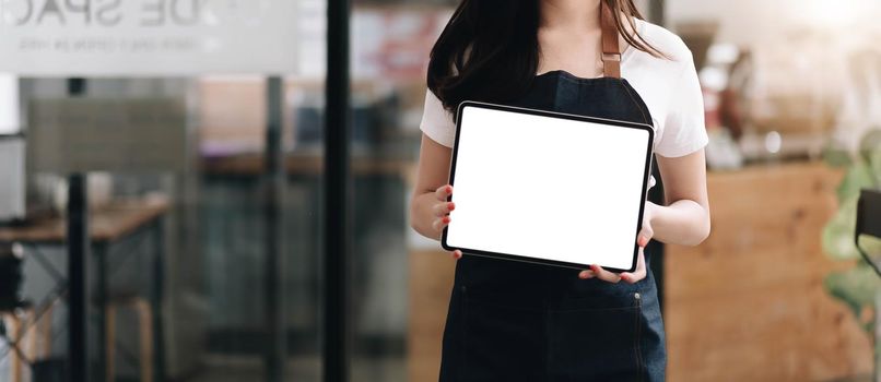 Close up on blank tablet computer that barista show and holding with two hand in front of coffee shop counter bar,Mock up space for display of menu or design..