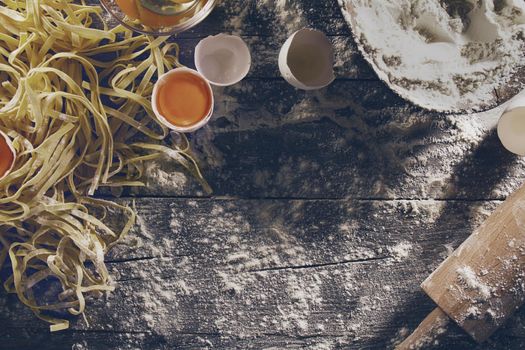 Process of cooking pasta with raw fresh ingredients for classic italian food - raw eggs, flour on wooden table. Top View. Toning.