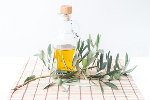 Glass bottle of olive oil and some olives with leaves isolated on a white background.