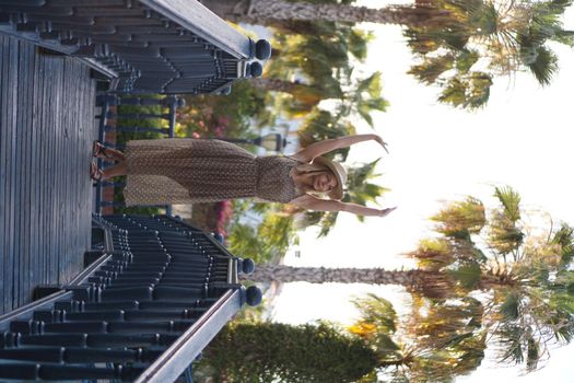 A girl in a dress and hat stands on the bridge. Palm trees on the background. Park on the coast of Alanya Turkey