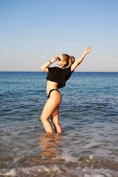 Young woman in a black tank top and underpants on the sea beach. Tanned body, body positive. Vertical photo