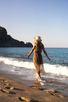 Woman on the beach in a brown dress and with a straw hat. Vacation on the beach of Turkey