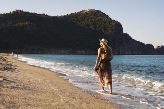 Woman on the beach in a brown dress and with a straw hat. Vacation on the beach of Turkey