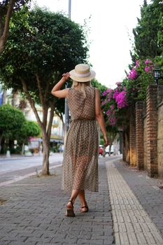 Young pretty girl walking on the summer turkey street. Vertical photo. A woman in a dress walks along a beautiful street with flowers. Alanya Turkey