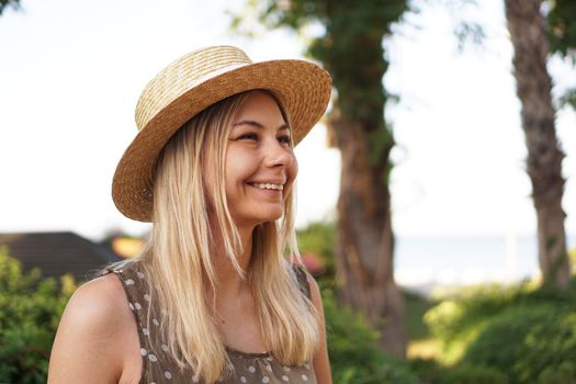 Portrait of a young blonde in a hat on a tropical background. Sunny light and bright colors.