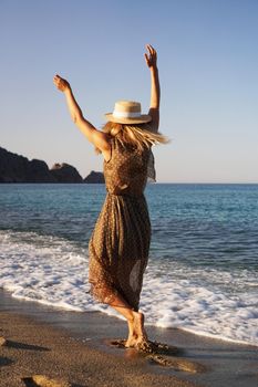 Woman on the beach in a brown dress and with a straw hat. Vacation on the beach of Turkey