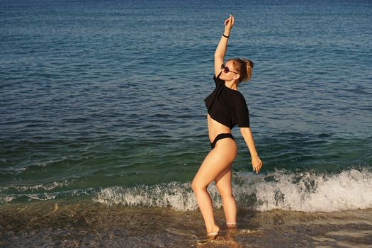 Young woman in a black tank top and underpants on the sea beach. Tanned body, body positive