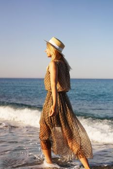 Woman on the beach in a brown dress and with a straw hat. Vacation on the beach of Turkey