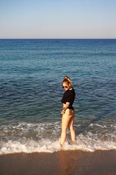 Young woman in a black tank top and underpants on the sea beach. Tanned body, body positive. Vertical photo