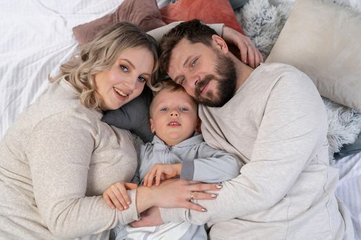 Happy family concept Mother father and little son have fun at home Caucasian family indoors Pregnant mom beard dad and funny little boy lie on the couch