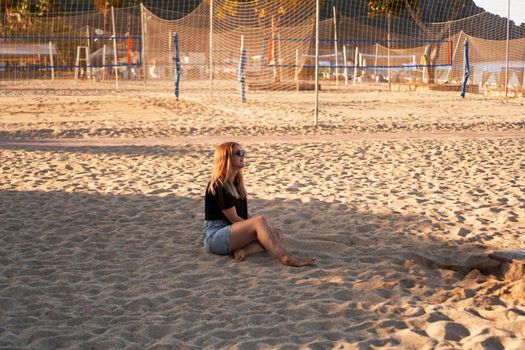 Woman at the summer beach in a hot day. Nearby there are palm trees and a sports volleyball court.