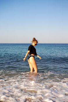 Young woman in a black tank top and underpants on the sea beach. Tanned body, body positive. Vertical photo