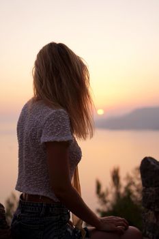 The girl looks at the sea sunset from a high point. Vertical photo with woman back