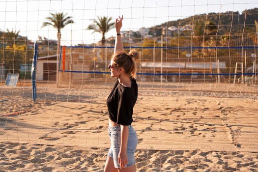 Portrait of attractive woman near volleyball net on the beach. Beautiful young woman in shorts, black tank top and sunglasses. Against the background of the beach and palms