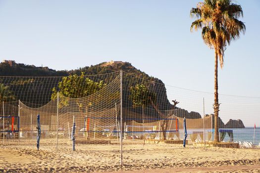 Volleyball court on the beach in Alanya, Turkey. Hot weather, palms and mountains on the background. Tall palm tree over the sea