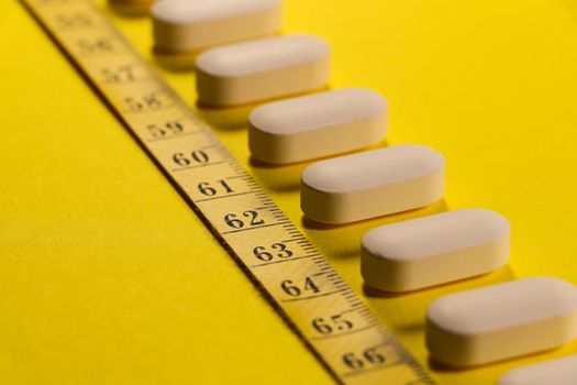 White tablet pills with measuring tape on bright yellow abstract weight-loss concept