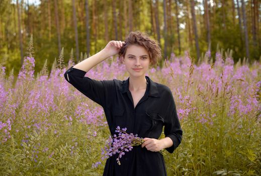 Young woman with a bouquet of lupines in her hand against the background of blooming Ivan-tea. Soft selective focus