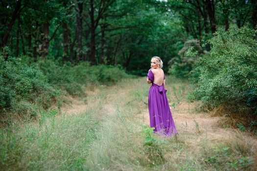 Girl model blonde in a lilac dress with a bouquet with a green forest