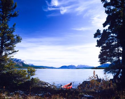 Red canoe on boreal forest taiga wilderness shore of beautiful calm Tagish Lake, Yukon Territory, Canada