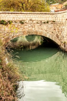 The Jucar River and old stone bridge surrounded by vegetation in Alcala del Jucar village