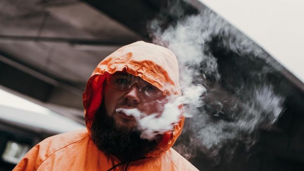 A man in safety glasses and an orange suit. Man exhales smoke. Protection air pollution in the chemical industry