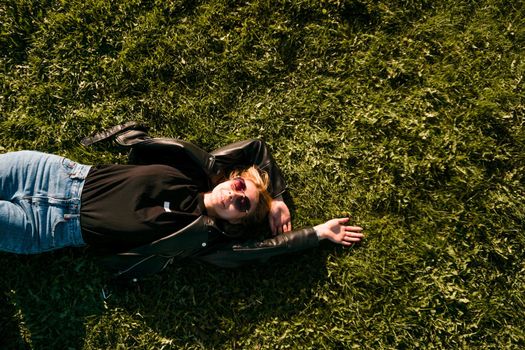 Beautiful healthy Young Woman lying and relaxing on the green grass. Happy smiling blonde in sunglasses on a summer day.