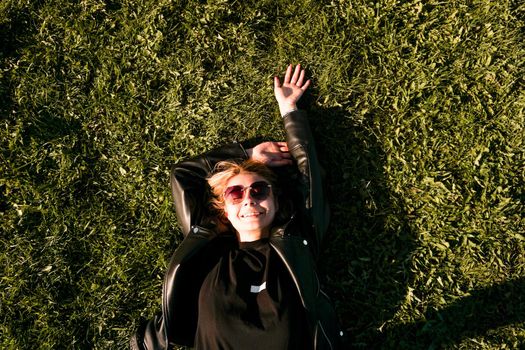 Beautiful healthy Young Woman lying and relaxing on the green grass. Happy smiling blonde in sunglasses on a summer day.