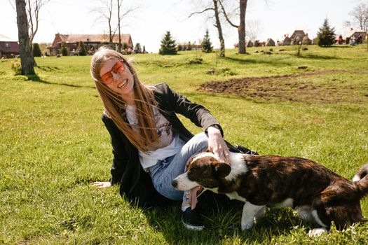 Young woman in red sunglasses plays with her corgi on a summer green lawn. Sunny day. Happy pet and owner