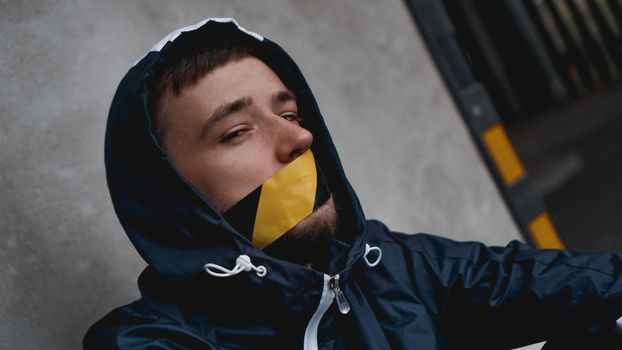 Man with tape over his mouth. The mouth is sealed with warning tape