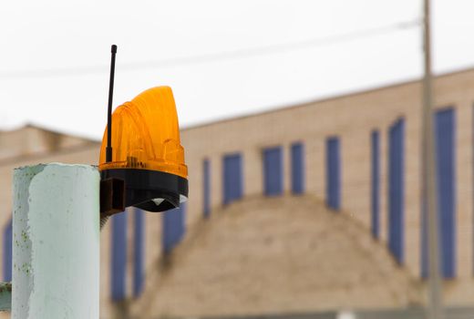 Alarm beacon with antenna for transmitting the alarm signal on the pipe. Signal lamp on a metal pole against the background of the house. The concept of industry, construction, health and safety.