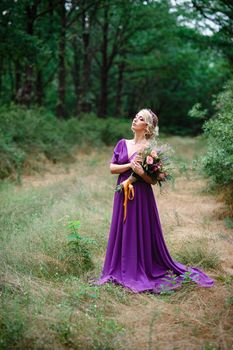 Girl model blonde in a lilac dress with a bouquet with a green forest