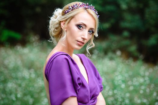 Girl model blonde in a lilac dress with a bouquet with a green forest