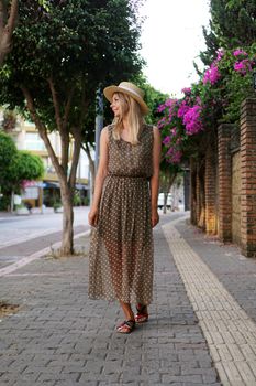 Young pretty girl walking on the summer turkey street. Vertical photo. A woman in a dress walks along a beautiful street with flowers. Alanya Turkey