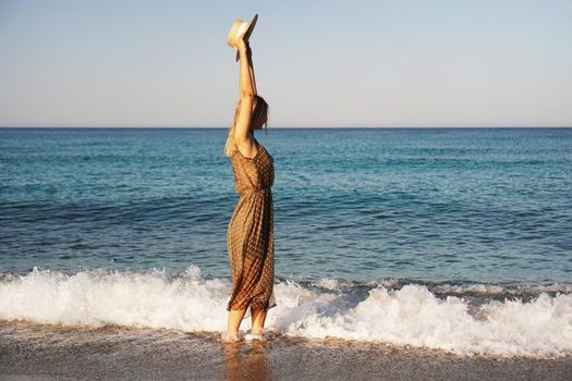 Woman on the beach in a brown dress and with a straw hat. Vacation on the beach of Turkey