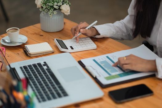 Close up Businesswoman or accountant using calculator and laptop for calaulating finance, tax, accounting, statistics and analytic research concept