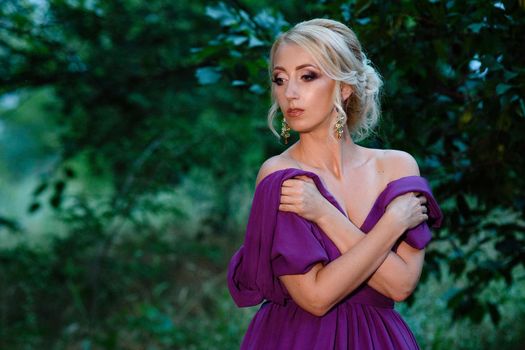 Girl model blonde in a lilac dress with a bouquet with a green forest