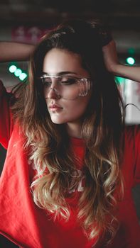 Pretty young woman in red hoodie sitting on car parking. Wearing stylish urban outfit