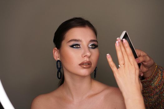 Make up artist taking mobile photo for the model with blue fashion makeup