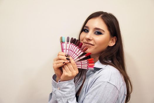 Pretty young woman smiling, holding a manicure and pedicure nail polish palette in a hand. Cosmetic products. Beauty salon.