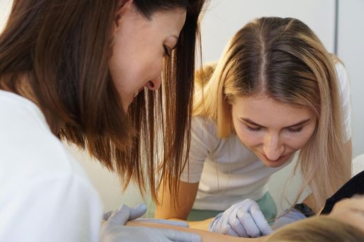 Two cheerful confident cosmetologists doing hair removal. Two happy women do the armpit depilation procedure. The concept of teaching depilation