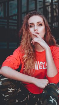 Fashion model wearing red hoodie with the inscription los angeles posing in the city at parking. Fashion urban outfit. Casual everyday clothing style